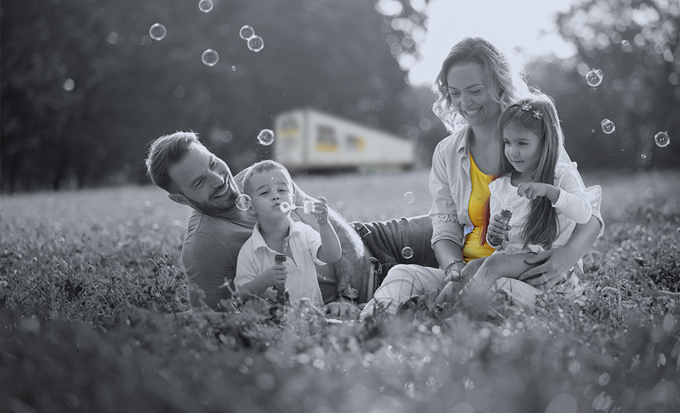 Family playing in the grass, blowing bubbles, with XTL transport truck in the background