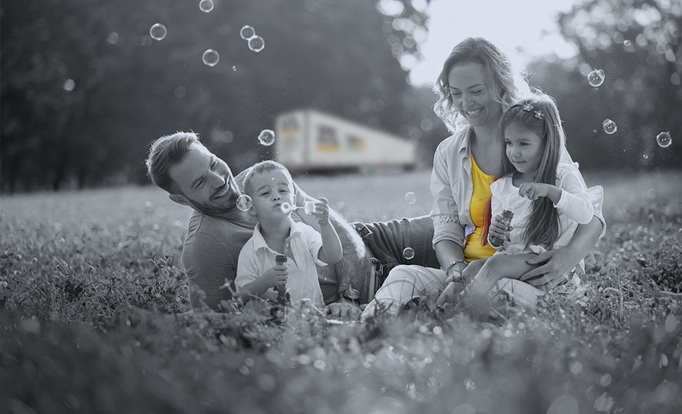 Famille jouant sur l’herbe à faire des bulles, avec un camion XTL en arrière-plan