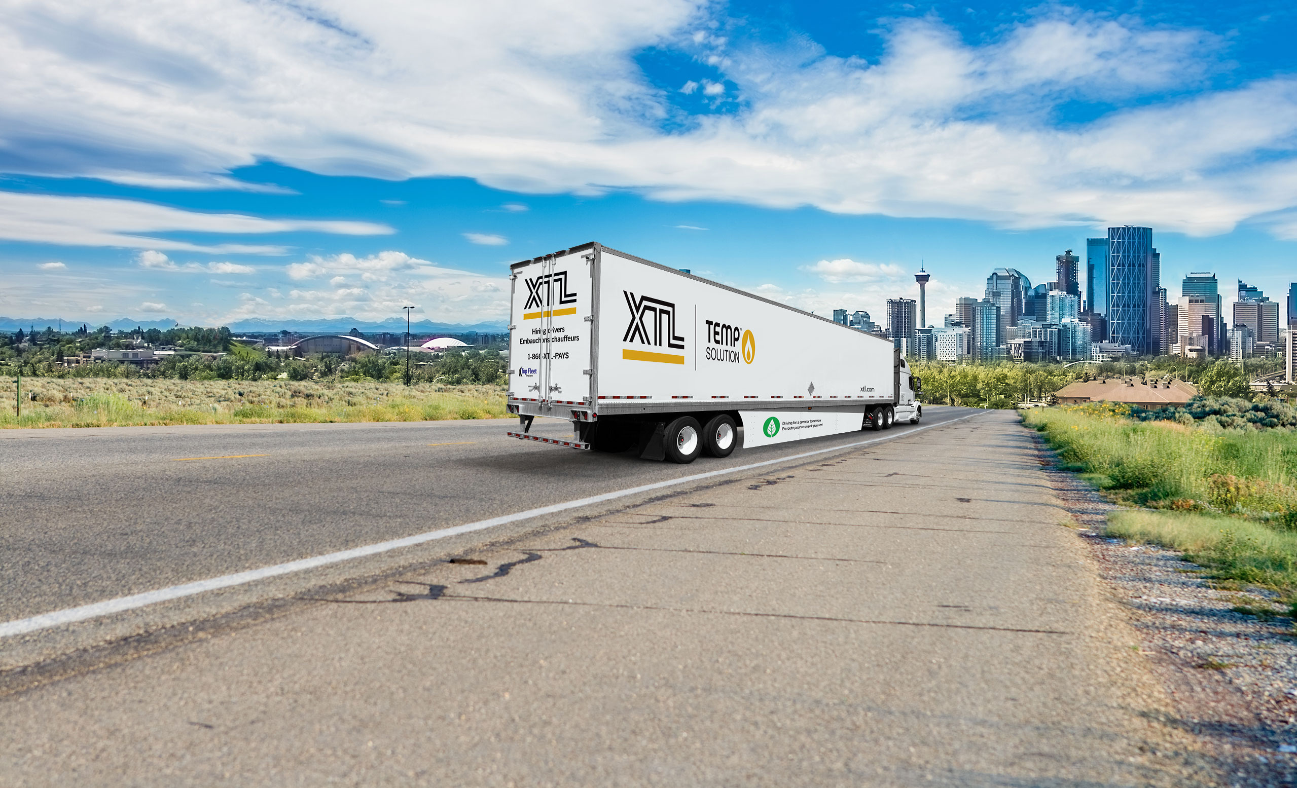 XTL transport truck and trailer driving on road, with city of Calgary in the background