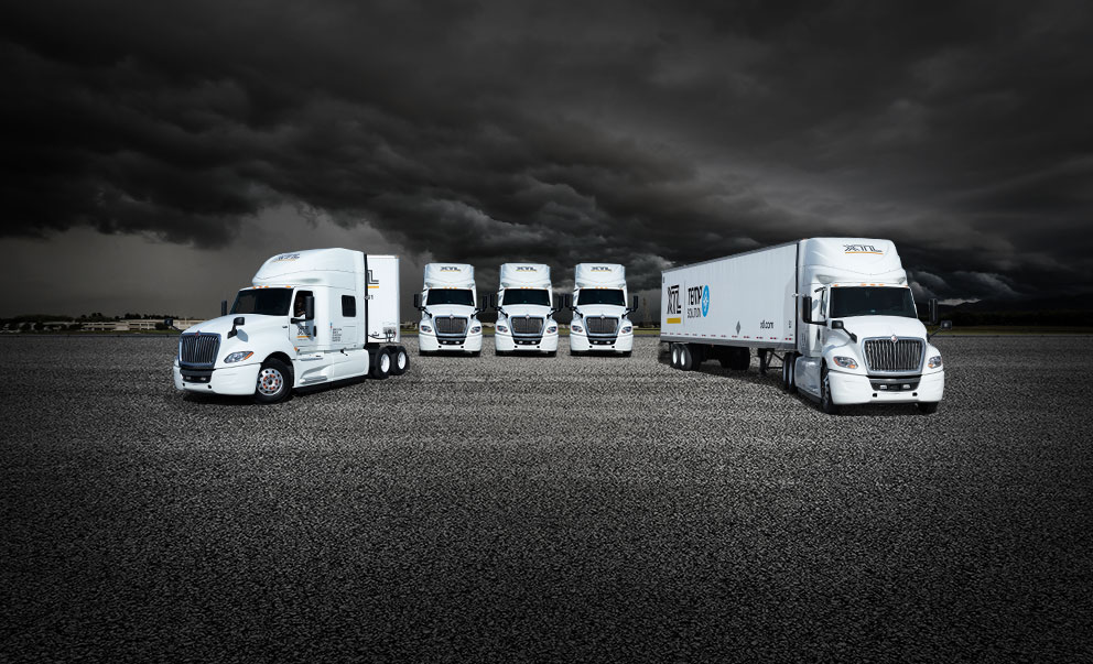 Five XTL transport trucks parked in paved yard