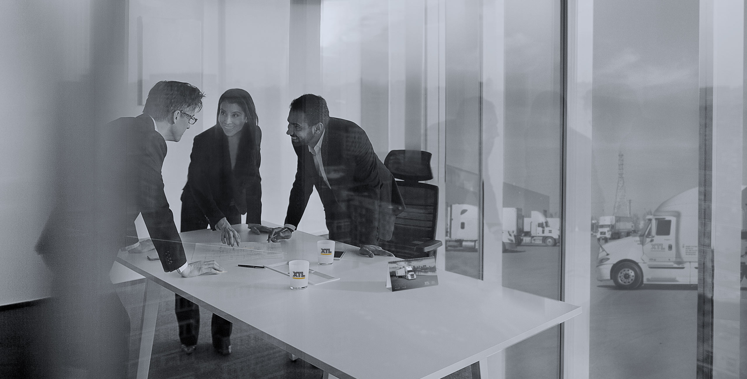 Three business people standing around XTL boardroom table with XTL trucks outside of the windows