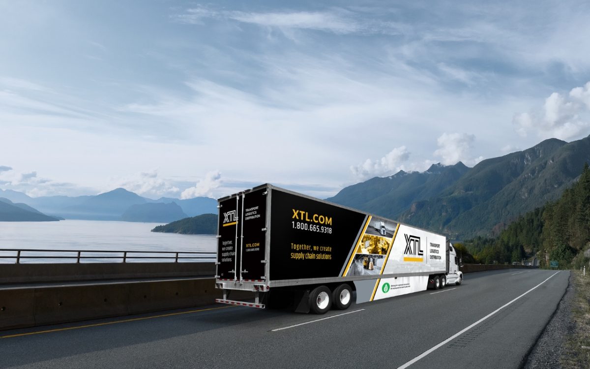 Semi truck featuring XTL branding travelling along a curved highway by the shoreline, showcasing quality transportation services against a peaceful mountain landscape.